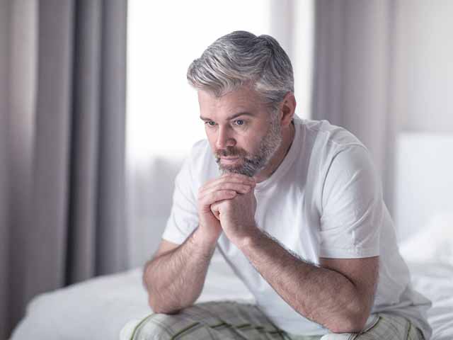 Man who suffers from both low libido and erectile dysfunction, sitting on the bed, looking concerned